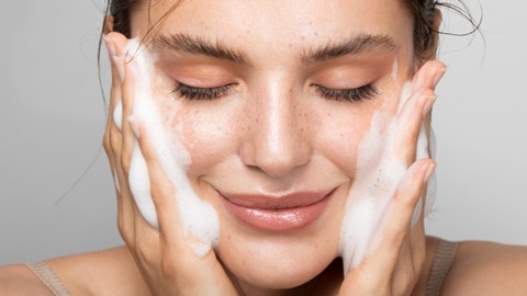 Une jeune femme frotte son visage à deux mains avec un soin cosmétique moussant